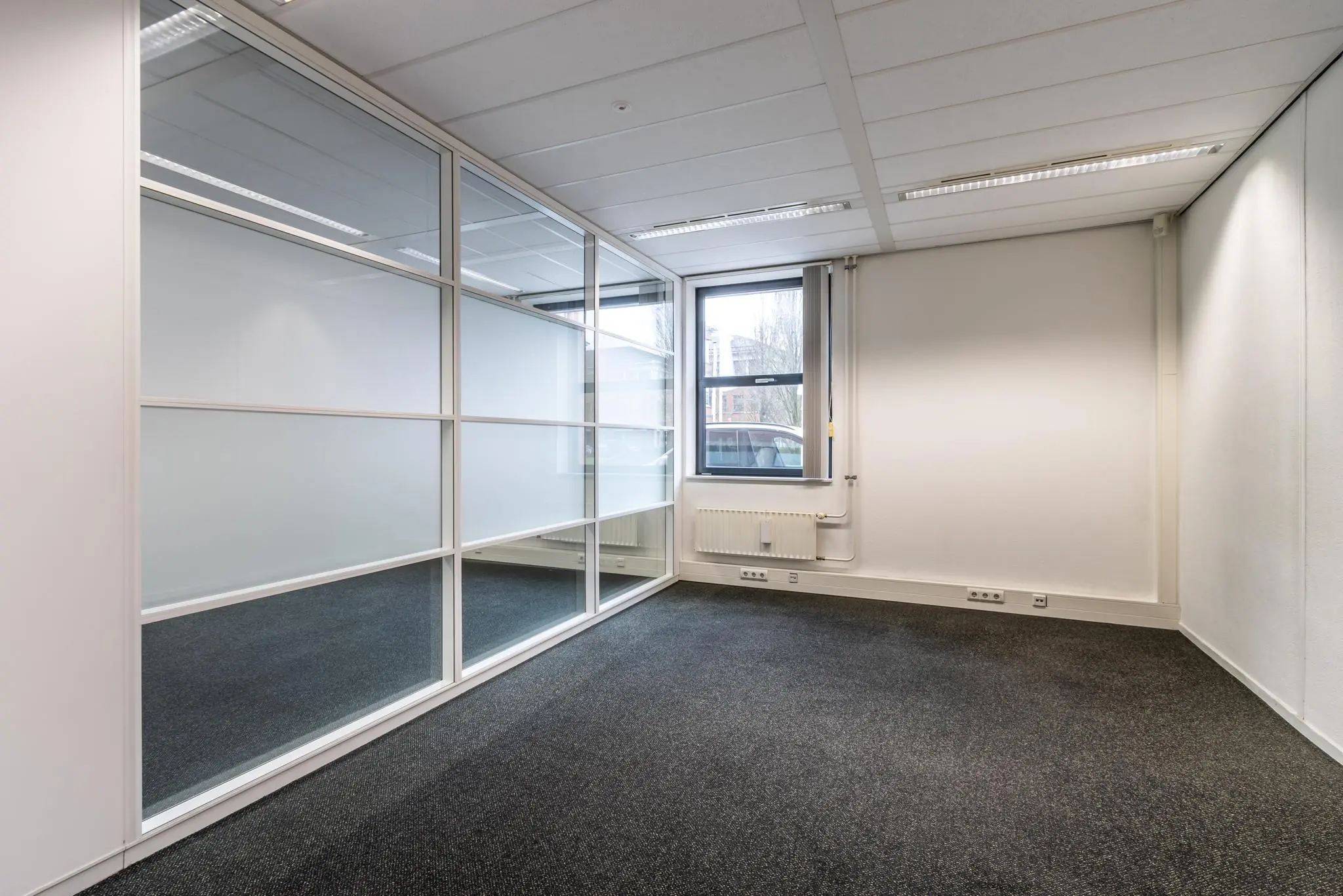 Leeg kantoor met glazen scheidingswand aan de Lange Dreef, voorzien van raam en radiator.